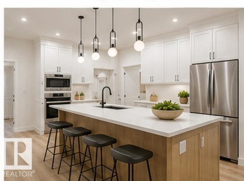 Kitchen featuring white shaker cabinetry, stainless steel appliances, a center island with light wood-finish paneling, white countertops, and wood-finish flooring - 3320 Chickadee Drive Nw, Edmonton, AB - Indoor Photo Showing Kitchen With Upgraded Kitchen