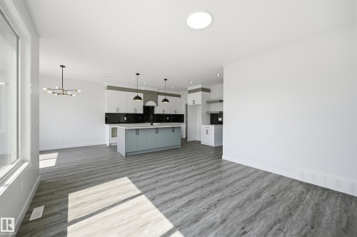 Open-concept living area featuring wood-finish flooring, a large kitchen island with light blue cabinetry, pendant lighting, and a modern chandelier - 3 Pierwyck Loop, Spruce Grove, AB - Indoor Photo Showing Other Room