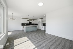 Open-concept living area featuring wood-finish flooring, a large kitchen island with light blue cabinetry, pendant lighting, and a modern chandelier - 