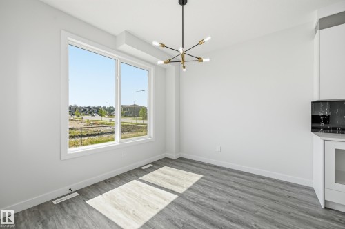 Bright interior space featuring a large picture window, a contemporary chandelier, wood-finish flooring, and a built-in microwave - 3 Pierwyck Loop, Spruce Grove, AB - Indoor Photo Showing Other Room