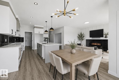 Open-concept living space featuring wood-finish flooring, a contemporary kitchen with white cabinetry and dark backsplash, a kitchen island with sink and pendant lighting, a dining area, and a living area with a fireplace - 3 Pierwyck Loop, Spruce Grove, AB - Indoor Photo Showing Dining Room With Fireplace