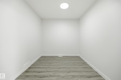 Room with neutral white walls, grey wood-finish flooring, white baseboards, and a flush-mount ceiling light fixture - 