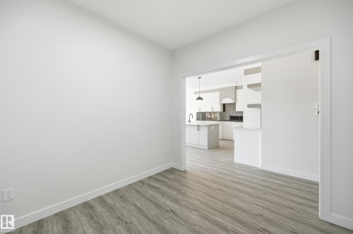Bright room with wood-finish flooring, white baseboards, and a wide entryway leading to a modern kitchen - 3 Pierwyck Loop, Spruce Grove, AB - Indoor Photo Showing Other Room