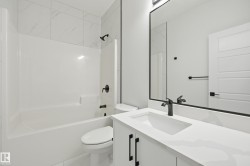 Bathroom featuring a white bathtub with a shower, white tile surround, and matte black fixtures - 