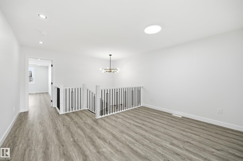 Bright upper-level landing with wood-finish flooring, modern metal and wood railing, recessed lighting, and a contemporary chandelier - 3 Pierwyck Loop, Spruce Grove, AB - Indoor Photo Showing Other Room