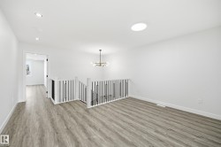 Bright upper-level landing with wood-finish flooring, modern metal and wood railing, recessed lighting, and a contemporary chandelier - 