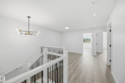 Upper-level landing featuring wood-finish flooring, a contemporary chandelier, recessed lighting, and a white and black stair railing - 