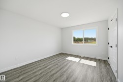 Bright interior room featuring a large window, wood-finish flooring, white walls, a flush-mount ceiling light, and a paneled door with matte black hardware - 