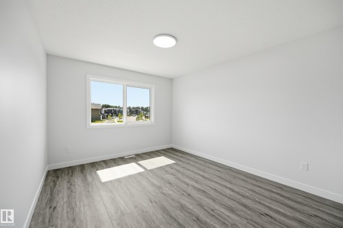Room featuring wood-finish flooring, a white ceiling with a flush-mount light fixture, and a large window providing outdoor scenery - 3 Pierwyck Loop, Spruce Grove, AB - Indoor Photo Showing Other Room