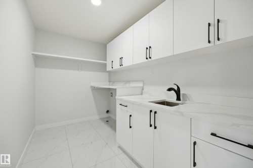 Laundry area featuring a large single-basin sink with a matte black pull-down faucet, white cabinetry with black hardware, white countertops with subtle veining, and large format floor tiles - 3 Pierwyck Loop, Spruce Grove, AB - Indoor