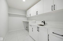 Laundry area featuring a large single-basin sink with a matte black pull-down faucet, white cabinetry with black hardware, white countertops with subtle veining, and large format floor tiles - 
