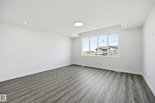 Spacious room featuring wood-finish flooring, a large window, recessed lighting, a ceiling-mounted light fixture, and white baseboards - 3 Pierwyck Loop, Spruce Grove, AB - Indoor Photo Showing Other Room