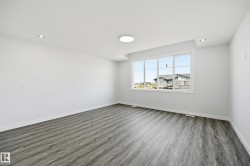 Spacious room featuring wood-finish flooring, a large window, recessed lighting, a ceiling-mounted light fixture, and white baseboards - 