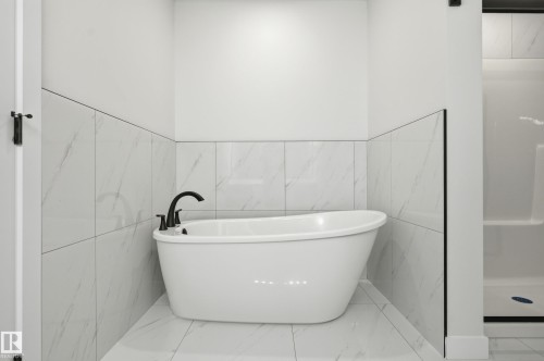 Freestanding soaking tub with matte black fixtures, set against white tile walls with subtle veining - 3 Pierwyck Loop, Spruce Grove, AB - Indoor Photo Showing Bathroom