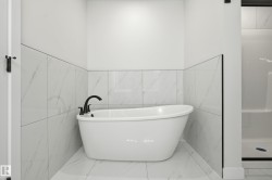 Freestanding soaking tub with matte black fixtures, set against white tile walls with subtle veining - 