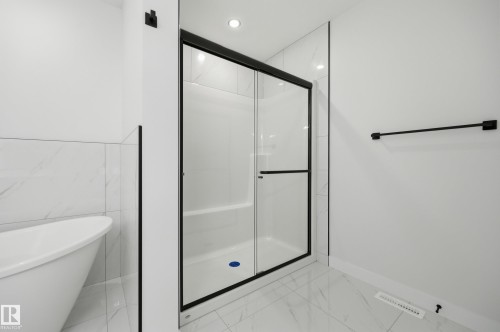 White tiled bathroom featuring a walk-in shower with black-framed glass doors and a freestanding tub - 3 Pierwyck Loop, Spruce Grove, AB - Indoor