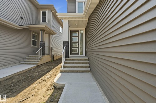 Modern facade featuring a dark entry door with frosted glass inserts, a covered front porch with white pillars, and a multi-level concrete walkway - 3 Pierwyck Loop, Spruce Grove, AB - Outdoor