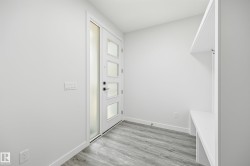 Entryway featuring a modern door with obscured glass panels, a built-in bench, overhead shelving, integrated coat hooks, and wood-finish flooring - 