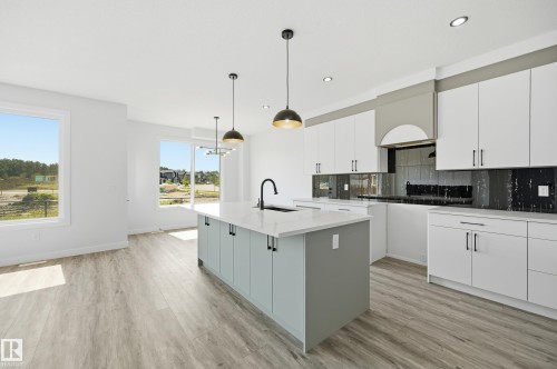 Open-concept kitchen featuring a light gray island with an integrated sink, white perimeter cabinetry with black hardware, a reflective black backsplash, and recessed lighting - 3 Pierwyck Loop, Spruce Grove, AB - Indoor Photo Showing Kitchen With Upgraded Kitchen