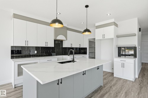 Modern kitchen featuring a large central island with a waterfall-edge countertop, black undermount sink, and matte black faucet - 3 Pierwyck Loop, Spruce Grove, AB - Indoor Photo Showing Kitchen With Upgraded Kitchen