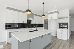 Modern kitchen featuring a large central island with a waterfall-edge countertop, black undermount sink, and matte black faucet - 