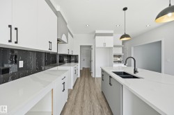 Modern kitchen featuring white cabinetry with matte black hardware, white countertops, and a black marble-effect backsplash - 