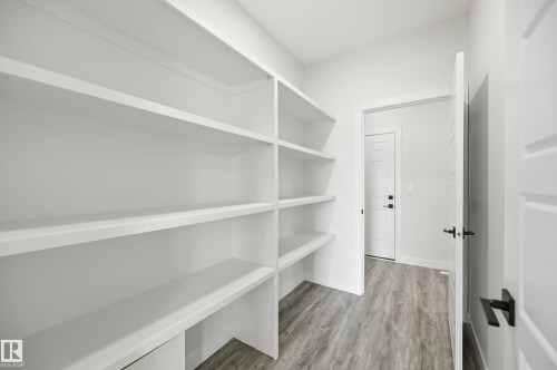 Spacious pantry featuring extensive built-in shelving, durable wood-finish flooring, and white paneled doors with matte black hardware - 3 Pierwyck Loop, Spruce Grove, AB - Indoor With Storage