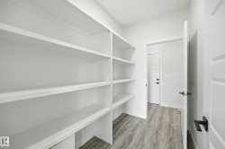 Spacious pantry featuring extensive built-in shelving, durable wood-finish flooring, and white paneled doors with matte black hardware - 