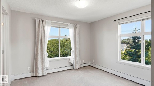 Carpeted interior room featuring two large windows, baseboard heating, and a flush mount ceiling light fixture - #361 7805 71 St Nw, Edmonton, AB - Indoor Photo Showing Other Room