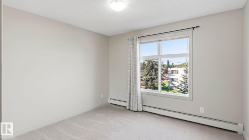Room featuring a large window, light gray walls, textured carpet, and baseboard heating - #361 7805 71 St Nw, Edmonton, AB - Indoor Photo Showing Other Room
