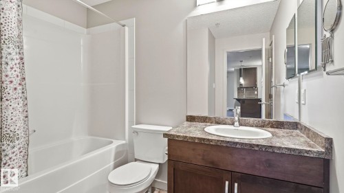 Bathroom featuring a full-size bathtub with integrated shower, single-piece toilet, and a vanity with a drop-in sink and dark wood-finish cabinetry - #361 7805 71 St Nw, Edmonton, AB - Indoor Photo Showing Bathroom
