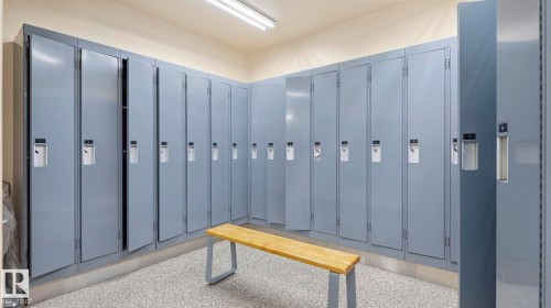 Locker room featuring multiple full-height metal lockers, suspended fluorescent lighting, and durable speckled flooring - #361 7805 71 St Nw, Edmonton, AB - Indoor Photo Showing Other Room