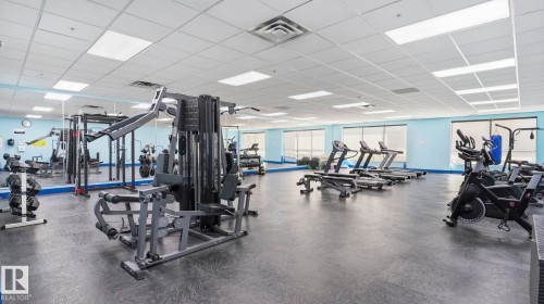 Fitness center featuring multiple exercise machines, mirrored walls, and resilient rubber flooring - #361 7805 71 St Nw, Edmonton, AB - Indoor Photo Showing Gym Room