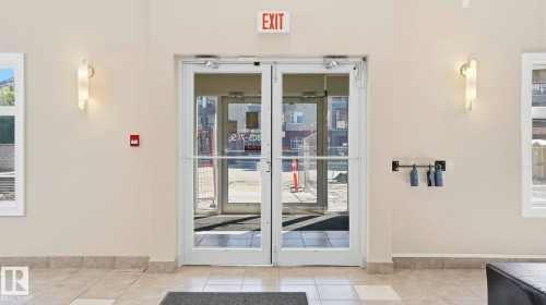 Double glass doors with polished handles, neutral wall paint, and sconce lighting - #361 7805 71 St Nw, Edmonton, AB - Indoor Photo Showing Other Room