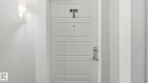 White paneled door with brushed nickel hardware, featuring a modern wall sconce and textured wall finish - #361 7805 71 St Nw, Edmonton, AB -  Photo Showing Other Room