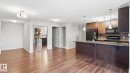Open-concept living space featuring wood-finish flooring, a kitchen island with stone countertop, stainless steel sink with gooseneck faucet, black appliances, and pendant lighting - #361 7805 71 St Nw, Edmonton, AB  - Indoor Photo Showing Kitchen 