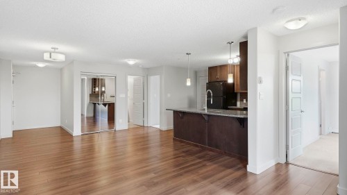 Open-concept living area with wood-finish flooring, recessed lighting, and a kitchen featuring dark cabinetry, a breakfast bar with stone countertop, and pendant lighting - #361 7805 71 St Nw, Edmonton, AB - Indoor