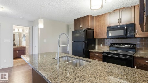 Kitchen featuring a granite island with dual basin sink, black appliances, subway tile backsplash, and wood-finish cabinetry - #361 7805 71 St Nw, Edmonton, AB - Indoor Photo Showing Kitchen With Double Sink