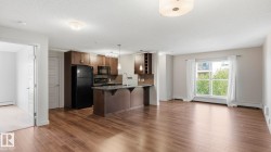Open-concept kitchen and living area featuring dark cabinetry with stainless steel appliances, a center island with breakfast bar, wood-finish flooring throughout, recessed ceiling lighting, and abundant natural light from multiple windows and glass doors - 
