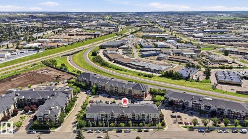 Aerial perspective showcasing the residential complex with multiple buildings, surrounding commercial properties, and a prominent highway system - #361 7805 71 St Nw, Edmonton, AB - Outdoor With View