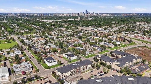 Aerial perspective showcasing a residential neighborhood with green spaces and a distant city skyline - #361 7805 71 St Nw, Edmonton, AB - Outdoor With View