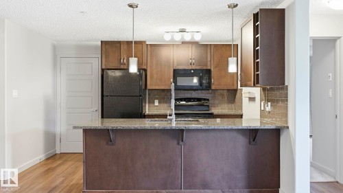 Kitchen featuring a peninsula with a stone-finish countertop, pendant lighting, stainless steel sink, and wood-finish cabinetry - #361 7805 71 St Nw, Edmonton, AB - Indoor Photo Showing Kitchen