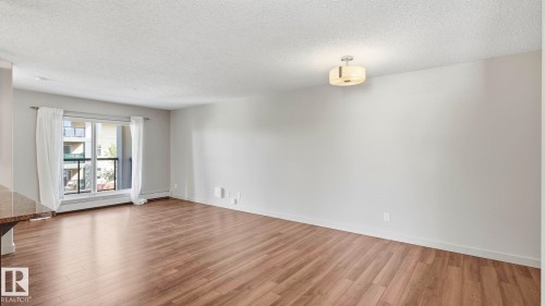 Open living area featuring wood-finish flooring, light grey painted walls, a built-in ceiling light fixture, and a glass-paned door opening to an outdoor balcony - #361 7805 71 St Nw, Edmonton, AB - Indoor Photo Showing Other Room