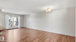 Open living area featuring wood-finish flooring, light grey painted walls, a built-in ceiling light fixture, and a glass-paned door opening to an outdoor balcony - 