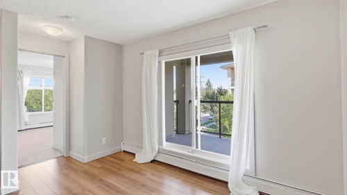 Room featuring wood-finish flooring, a sliding glass door to a balcony, and a doorway opening to a carpeted room with multiple windows - #361 7805 71 St Nw, Edmonton, AB - Indoor Photo Showing Other Room