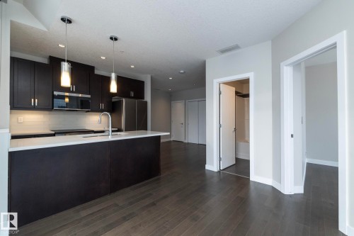 Modern kitchen featuring dark wood cabinetry, stainless steel appliances, white subway tile backsplash, and a large island with a composite countertop and integrated sink - #1201 10238 103 St Nw, Edmonton, AB - Indoor Photo Showing Kitchen With Upgraded Kitchen