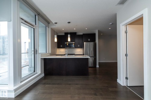 Kitchen featuring dark cabinetry, stainless steel appliances, a center island with pendant lighting, and light countertops - #1201 10238 103 St Nw, Edmonton, AB - Indoor Photo Showing Kitchen With Upgraded Kitchen