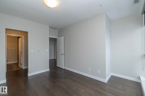 Spacious room featuring dark wood-finish flooring, light neutral-toned walls, and white baseboards - #1201 10238 103 St Nw, Edmonton, AB - Indoor Photo Showing Other Room