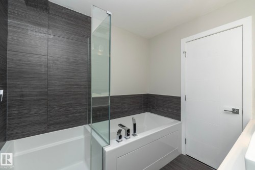 Contemporary bathroom featuring a bathtub with a glass shower partition, dark gray horizontally-textured wall tiling, and a square rain shower head - #1201 10238 103 St Nw, Edmonton, AB - Indoor Photo Showing Bathroom