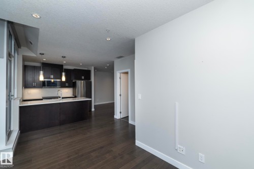 Open-concept kitchen featuring dark wood cabinetry, stainless steel appliances, a white countertop island with an undermount sink, and recessed lighting - #1201 10238 103 St Nw, Edmonton, AB - Indoor Photo Showing Kitchen
